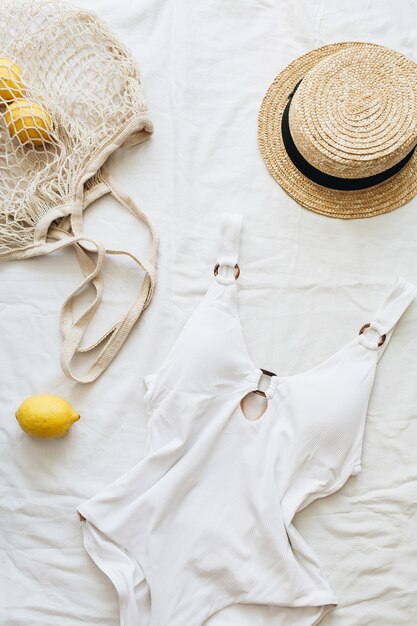 Composizione di moda da viaggio estivo. Costume da bagno donna, paglia e limoni in borsa a tracolla su fondo di lino. Disposizione piatta, vista dall'alto