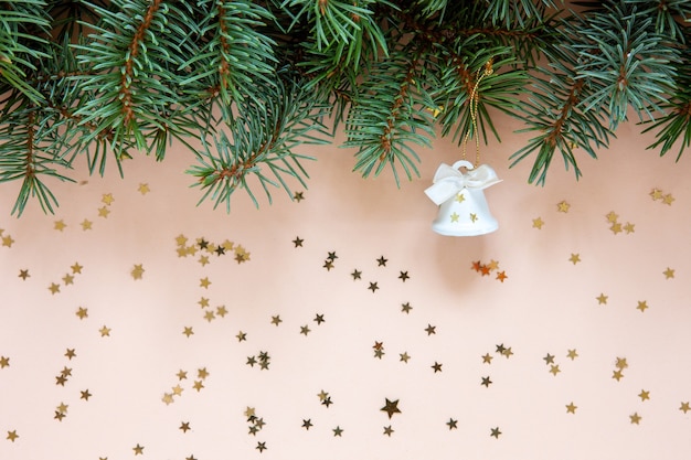 Composizione di Natale con rami di abete e campana di Natale. Primo piano, vista dall'alto su sfondo di colore pastello chiaro con coriandoli glitter dorati