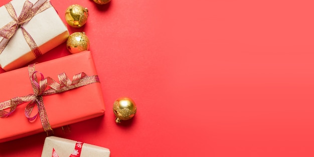 Composizione di Natale con scatola regalo rosso, nastri, palline rosse grandi e piccole, decorazioni natalizie su rosso. Vista piana, vista dall'alto, copyspace