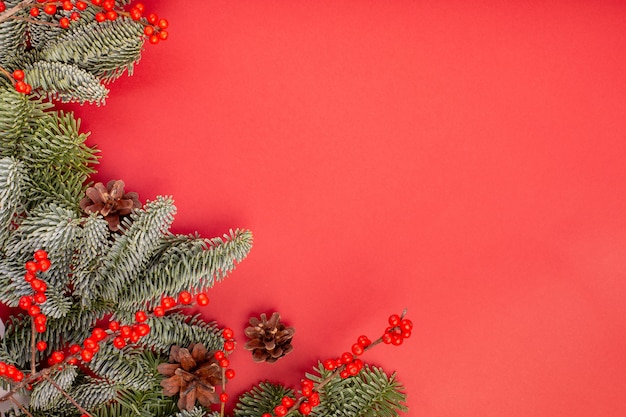 Composizione di Natale. Decorazioni natalizie rosse, rami di abete con protuberanze su sfondo rosso. Appartamento laico, vista dall'alto, copia dello spazio.