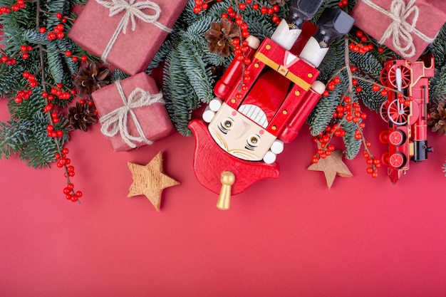 Composizione di natale. Decorazioni rosse di Natale, rami di abete con giocattoli, schiaccianoci, scatole regalo su sfondo rosso. Vista piana, vista dall'alto, copia spazio