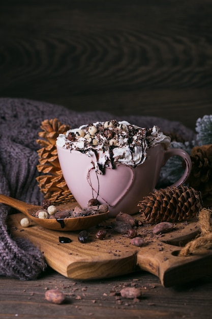 Composizione di Natale o Capodanno con cioccolata calda o bevanda al cacao con panna montata servita con cioccolato tritato e fave di cacao su piatto di legno rustico.