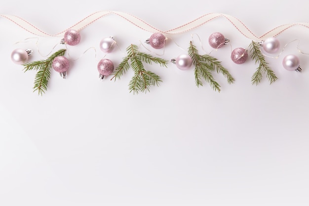 Composizione di Natale. Rami di abete, albero di natale, palla natalizia con decorazioni rosa di natale con nastro su sfondo bianco.