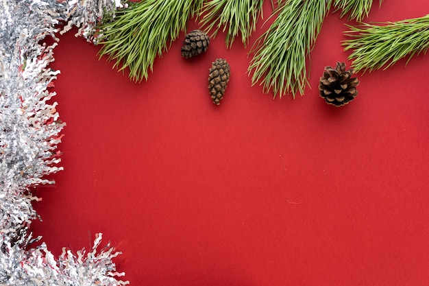 Composizione di Natale. Rami di abete e shishki con orpelli bianchi su sfondo rosso. Disposizione piatta, vista dall'alto, spazio per il testo