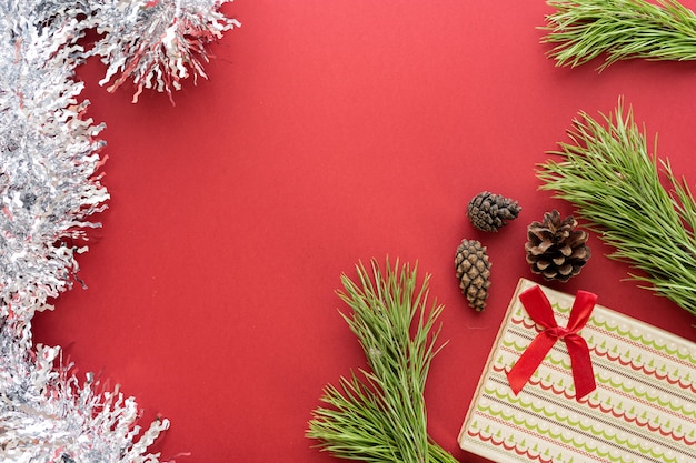 Composizione di Natale. Una scatola con un regalo e rami di abete rosso su sfondo rosso. Coni di abete e decorazioni natalizie. Disposizione piatta, vista dall'alto, spazio per il testo