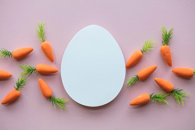 Composizione di Pasqua con l'uovo di Pasqua bianco in bianco e le carote del coniglietto di pasqua