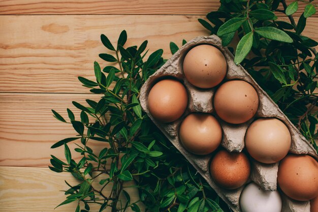 composizione di pasqua Le uova di Pasqua si trovano in una scatola di uova accanto a rami verdi su uno sfondo di legno chiaro foto di concetto di Pasqua dall'alto