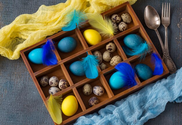 Composizione di Pasqua: nella scatola c&#39;erano uova blu, uova gialle, uova di quaglia e piume e posate - forchetta e cucchiaio