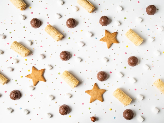 Composizione di pasticceria festosa dolce con cioccolato, cialde, biscotti, caramelle gommosa e molle e topping di pasta su uno sfondo bianco.