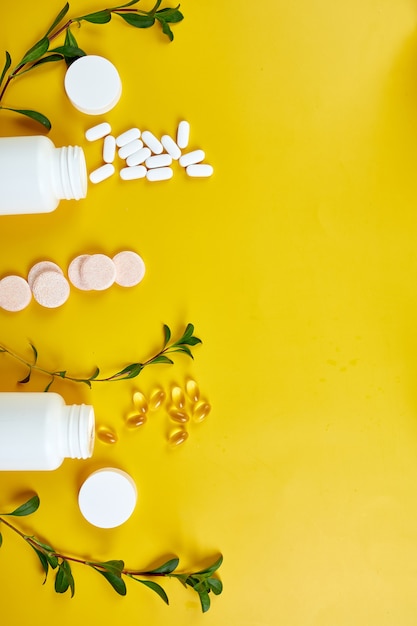Composizione di pillole, olio di pesce, vitamine con foglie verdi sulla superficie gialla