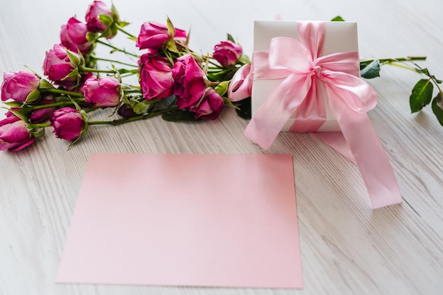 Composizione di roselline rosa confezione regalo cartolina su fondo di legno bianco Buon compleanno Biglietto di auguri per le vacanze San Valentino Festa della mamma delle donne Pasqua Spazio per il messaggio Invito a nozze