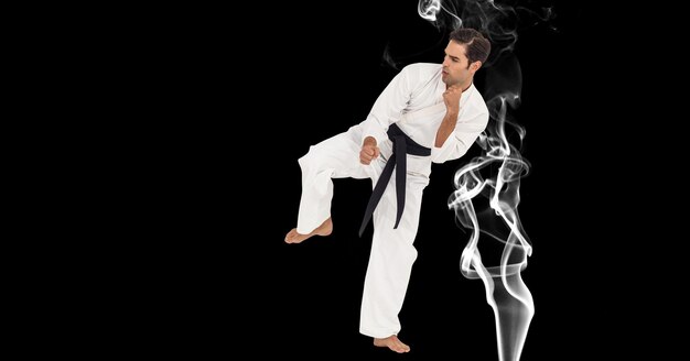 Composizione di un artista di karate marziale maschile con cintura nera che calcia sul fumo e copia spazio