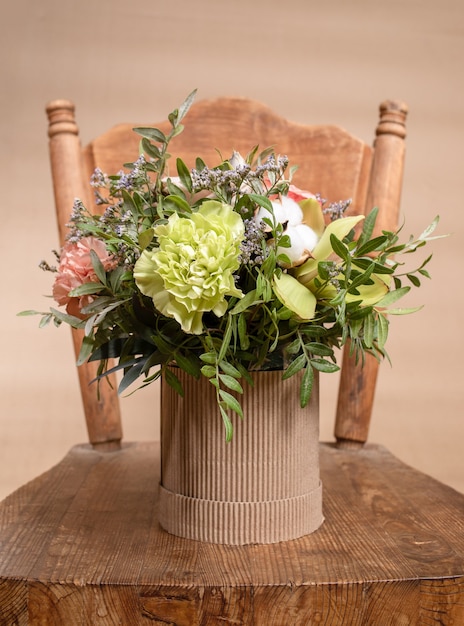 Composizione ecologica con bouquet di fiori in vaso di cartone fai da te in piedi sulla vecchia sedia in legno su sfondo beige.
