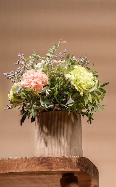 Composizione ecologica in stile Hygge con bouquet di fiori in vaso di cartone fai da te in piedi sul vecchio tavolo in legno su sfondo beige con spazio di copia.