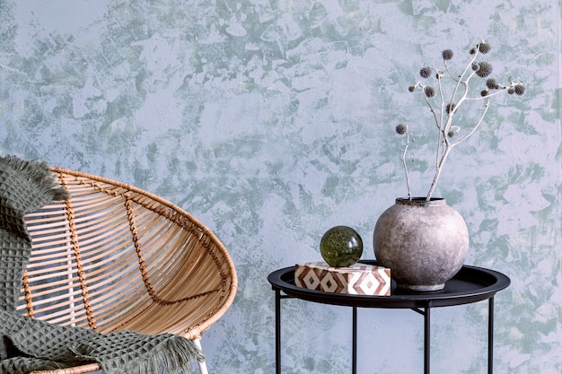 Composizione elegante di dettagli interni del soggiorno creativo e accogliente con poltrona in rattan e piante essiccate in vaso grigio