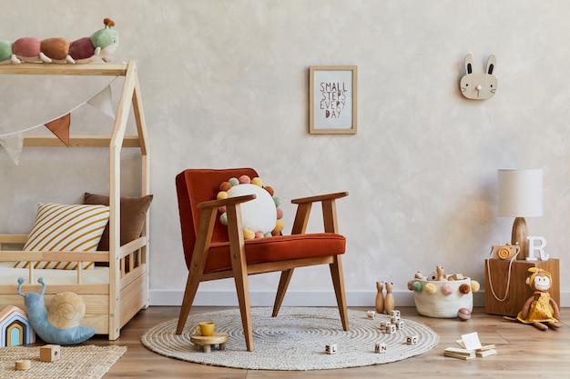 Composizione elegante di interni accoglienti della stanza del bambino scandinavo con letto in legno, poltrona rossa, peluche e giocattoli in legno e decorazioni tessili. Muro creativo. Copia spazio. Modello.