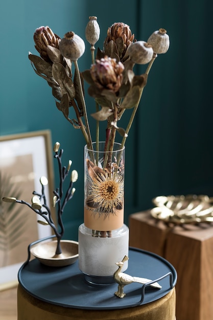 Composizione elegante e floreale di bellissimi fiori in vaso moderno sul pouf con accessori e mobili eleganti. Concetto di fiore in soggiorno. Pareti verdi. Interior design. Modello.