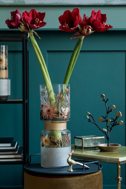 Composizione elegante e floreale di bellissimi fiori in vaso moderno sul pouf in velluto con accessori e mobili eleganti. Concetto di fiore in soggiorno. Pareti verdi. Interior design. Modello.