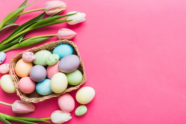 Composizione felice di Pasqua Uova di Pasqua in cesto su tavolo colorato con tulipani gialli Uova colorate naturali sfondo vista superiore con spazio di copia