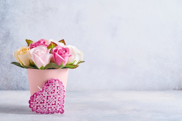 Composizione festiva con bellissimi fiori di rose delicate in scatola rotonda rosa con cuori rosa su sfondo grigio chiaro. Lay piatto, copia dello spazio.
