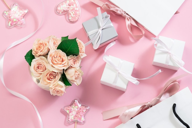 Composizione festiva con bouquet di rose rosa in vaso, decorazioni scintillanti, confezioni regalo