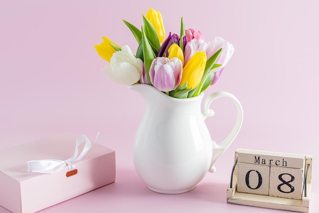 Composizione festiva di tulipani colorati in una scatola vacanza a brocca bianca e calendario in legno con la data della vacanza femminile di primavera