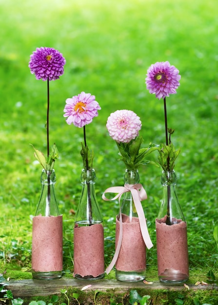 Composizione floreale con fiori di dalia rosa magenta viola rosa in bottiglie di vetro nel giardino