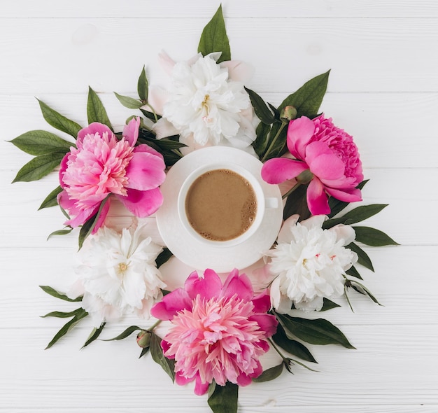 Composizione floreale di peonie rosa e bianche intorno a una tazza di caffè vista dall'alto