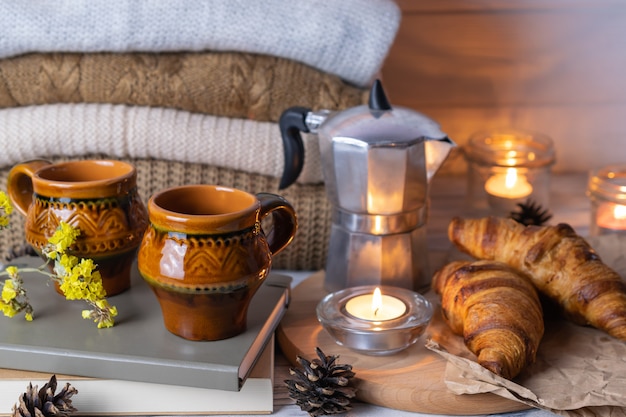 Composizione Hygge con due tazze di argilla rustica, cornetti, libri, candele e maglieria sul tavolo di legno