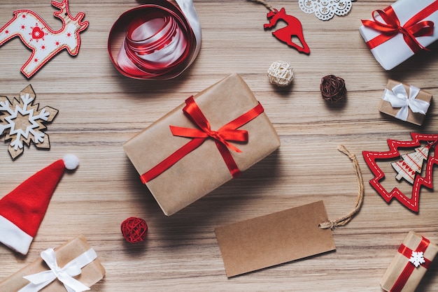 Composizione in Natale di giocattoli dell'albero di Natale, nastri e scatole regalo decorate sulla tavola di legno rustica. Etichetta di carta artigianale vuota per scrivere auguri di vacanza