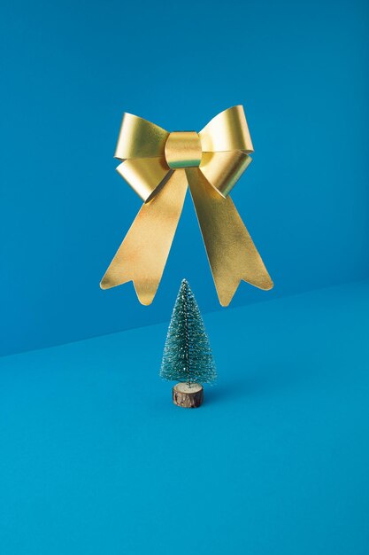 Composizione minimale con albero di Natale e grande nastro dorato che levita su sfondo blu