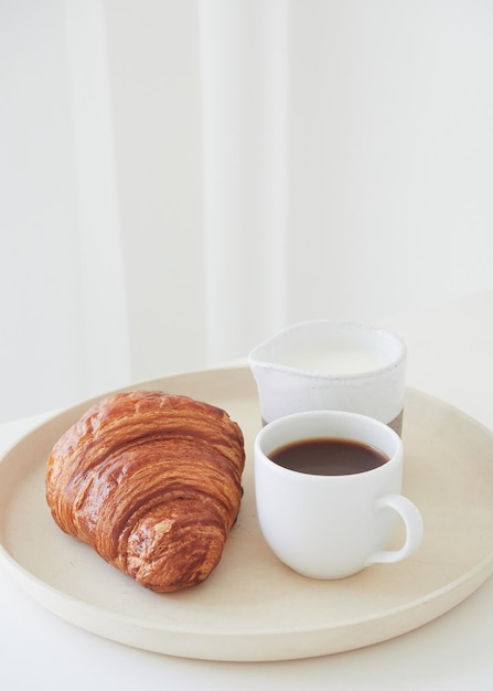 composizione monocromatica minimalista di un semplice piatto da colazione con tazza di caffè croissant e lattiera