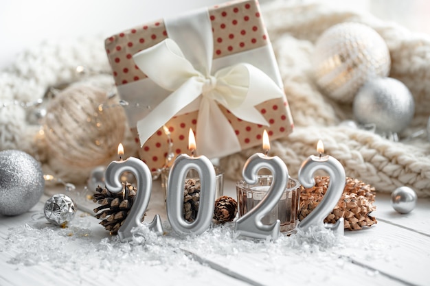 Composizione natalizia con candele a forma di numeri 2022, una confezione regalo e dettagli decorativi festivi su uno sfondo sfocato.