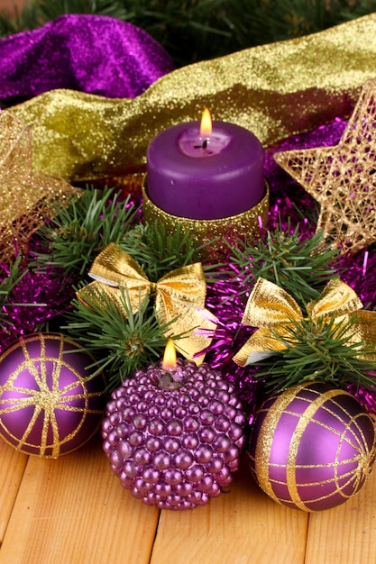 Composizione natalizia con candele e decorazioni nei colori viola e oro su tavola di legno