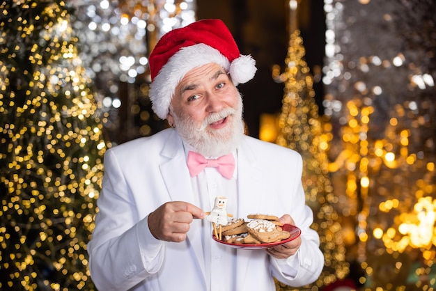 Composizione natalizia uomo d'affari senior in cappello di babbo natale l'illuminazione è ovunque biscotti fatti in casa per le vacanze amo l'uomo barbuto invernale tenere il giocattolo del pupazzo di neve fatto di cibo