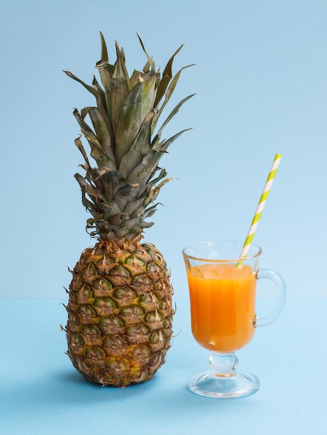 Composizione naturale con un ananas fresco e un bicchiere di succo di frutta su sfondo blu.