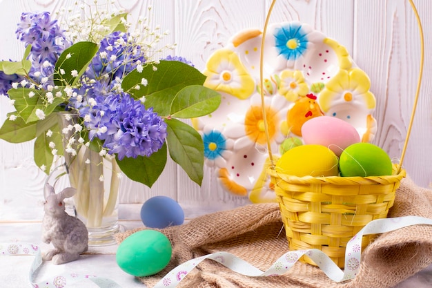 Composizione pasquale con uova colorate in un cesto di vimini una statuina di coniglio e un bouquet primaverile in a