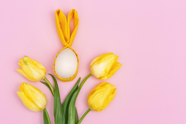 Composizione pasquale con uovo di pasqua con orecchie di coniglio e tulipano di fiori gialli freschi su rosa