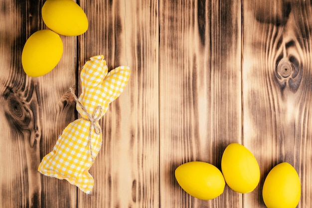 Composizione pasquale di cartolina d'auguri per le vacanze con sfondo in legno e uova di gallina colorate in giallo simpatico coniglietto bianco giallo fatto a mano con foulard Celebrazione evento tradizionale vacanza