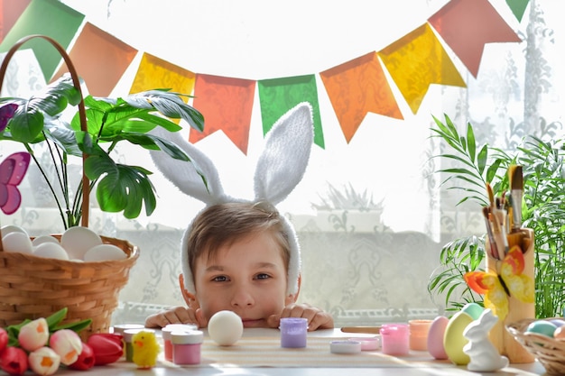 Composizione pasquale e un ragazzo con orecchie da coniglio si affaccia da dietro il tavolo Creatività per bambini