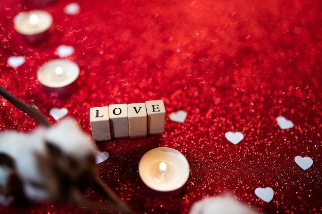 Composizione per San Valentino con la parola amore, candele, glitter e una pianta di cotone naturale