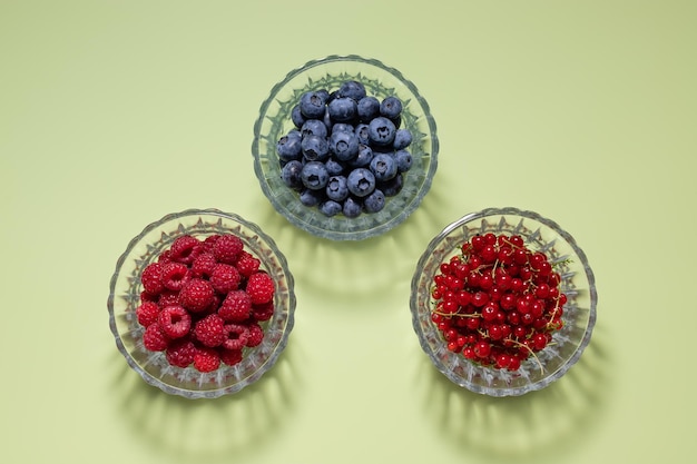 Composizione piatta con frutti di bosco freschi di stagione in ciotole di vetro su sfondo verde con ombre