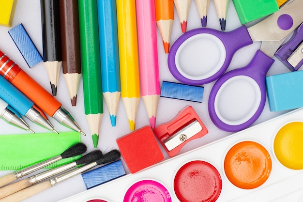 Composizione piatta con materiale scolastico su fondo di legno bianco dipinge matite in gomma per pennelli