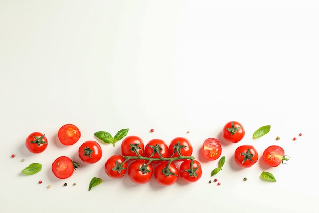 Composizione piatta laica con pomodorini freschi, pepe e basilico su spazio bianco, spazio per il testo. Verdure mature