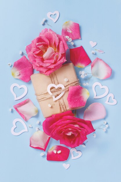 Composizione primaverile con rose, petali, cuori e confezione regalo su uno sfondo pastello