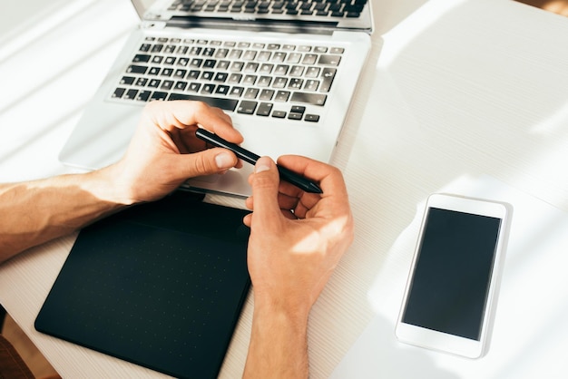 Composizione tecnologica vista dall'alto di gadget Belle mani dell'uomo con penna digitale accanto al computer portatile con schermo vuoto Processo di lavoro con penna digitale e tablet Concetto di tecnologia