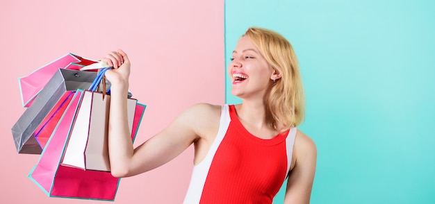 Compra tutto quello che vuoi. Ragazza soddisfatta dello shopping. La ragazza si diverte a fare shopping o ha appena ricevuto regali di compleanno. Il vestito rosso della donna tiene il mazzo dei sacchetti della spesa blu il fondo rosa. Suggerimenti per acquistare con successo le vendite.