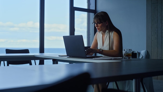 Computer di lavoro del responsabile dell'ufficio alla finestra panoramica Imprenditrice alla ricerca di computer portatile