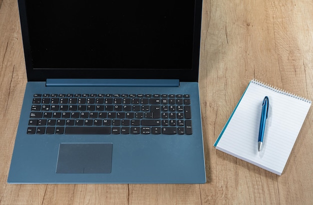 Computer portatile accanto a un blocco note vuoto e una penna su un tavolo da lavoro. Tecnologia, comunicazioni, concetto di homeoffice