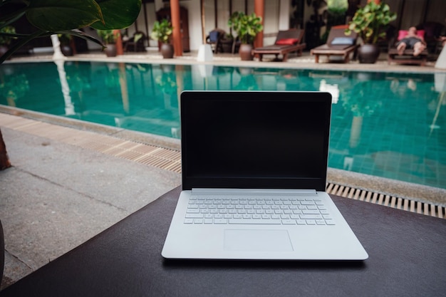 Computer portatile bianco sullo sfondo della piscina in un hotel esotico